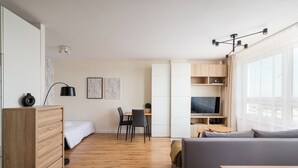 Een moderne, goed verlichte kamer met een houten vloer, een grijze bank, een houten dressoir, een eettafel met stoelen en een televisie.