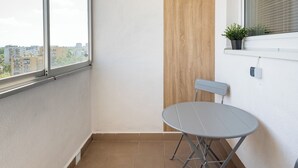 Een klein balkon met uitzicht op de stad, een wand van houten panelen, een tafeltje met een stoel en een bloempot.