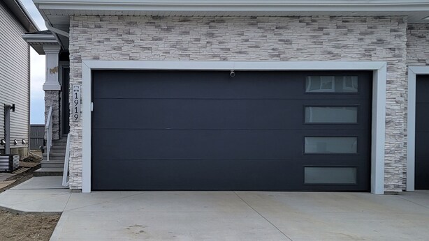 A modern two-story house with a stone facade, a dark garage door, and a clear sky. - Guest Suite in SouthWest Edmonton (Edmonton)