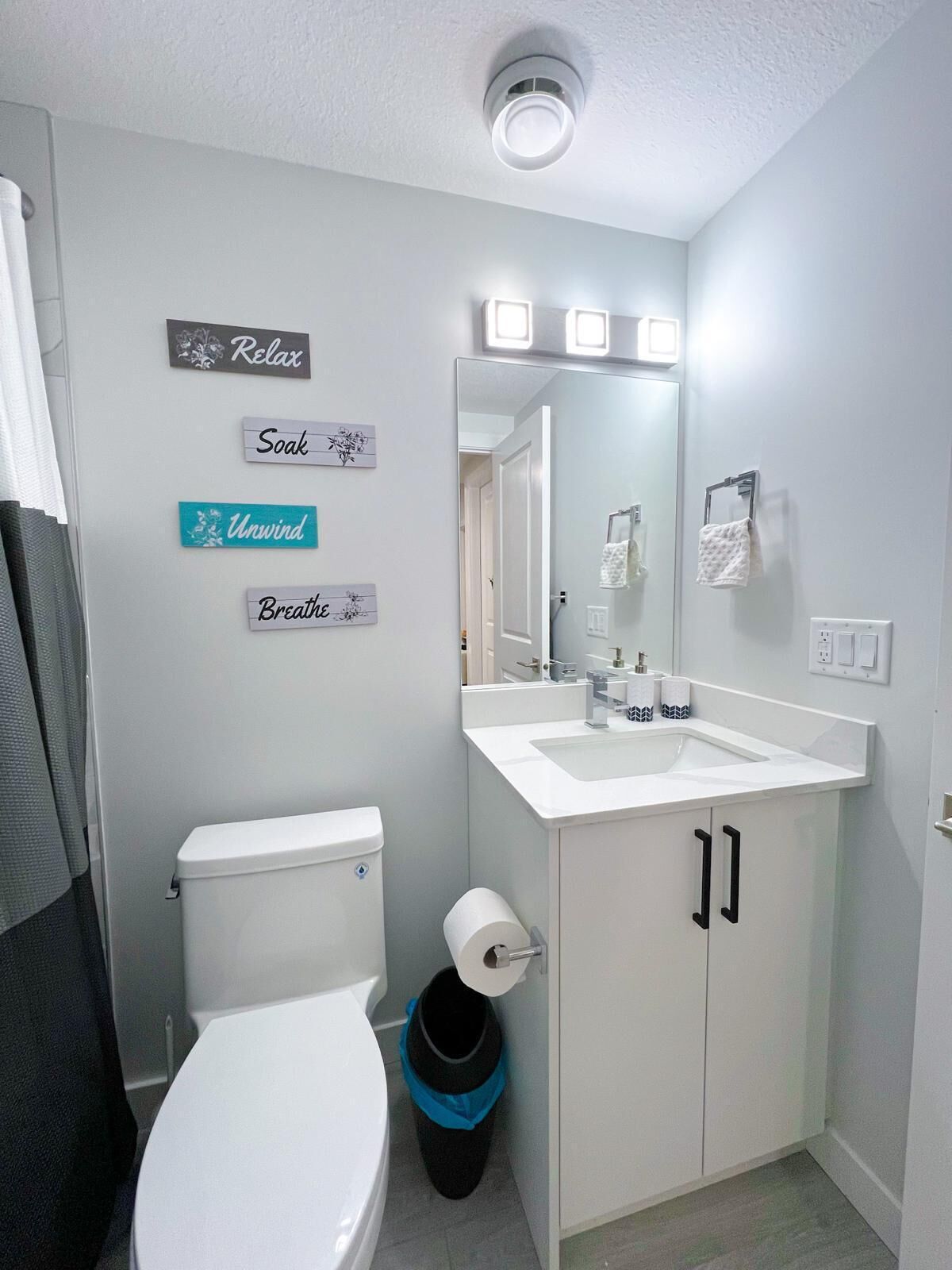 Une salle de bain équipée de toilettes, d’un lavabo et d’une poubelle. On y trouve des panneaux accrochés au mur avec des mots comme « Détendez-vous », « Relaxez-vous », « Reposez-vous » et « Respirez ».