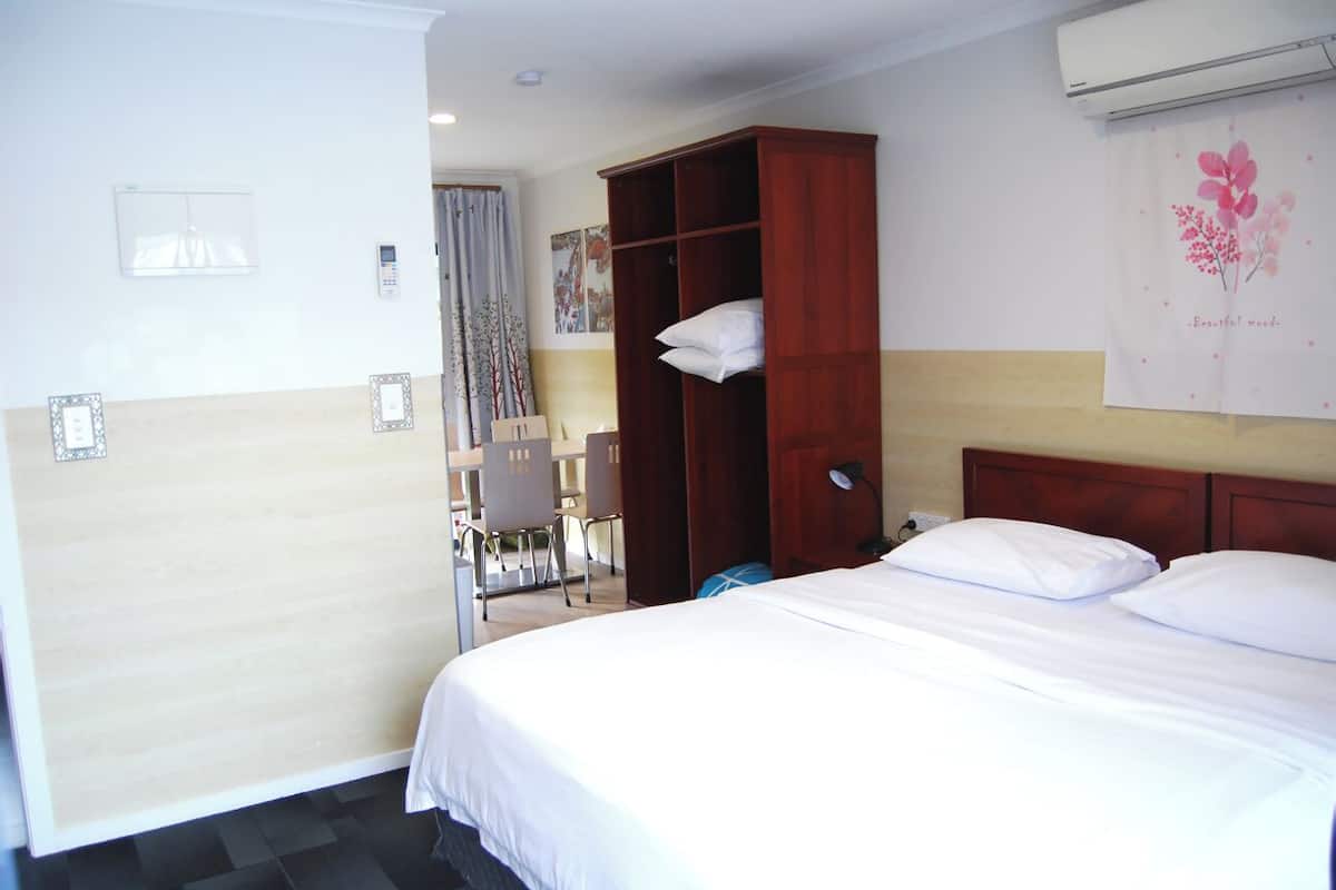A hotel room with a bed, a wooden wardrobe, a desk, and a chair.