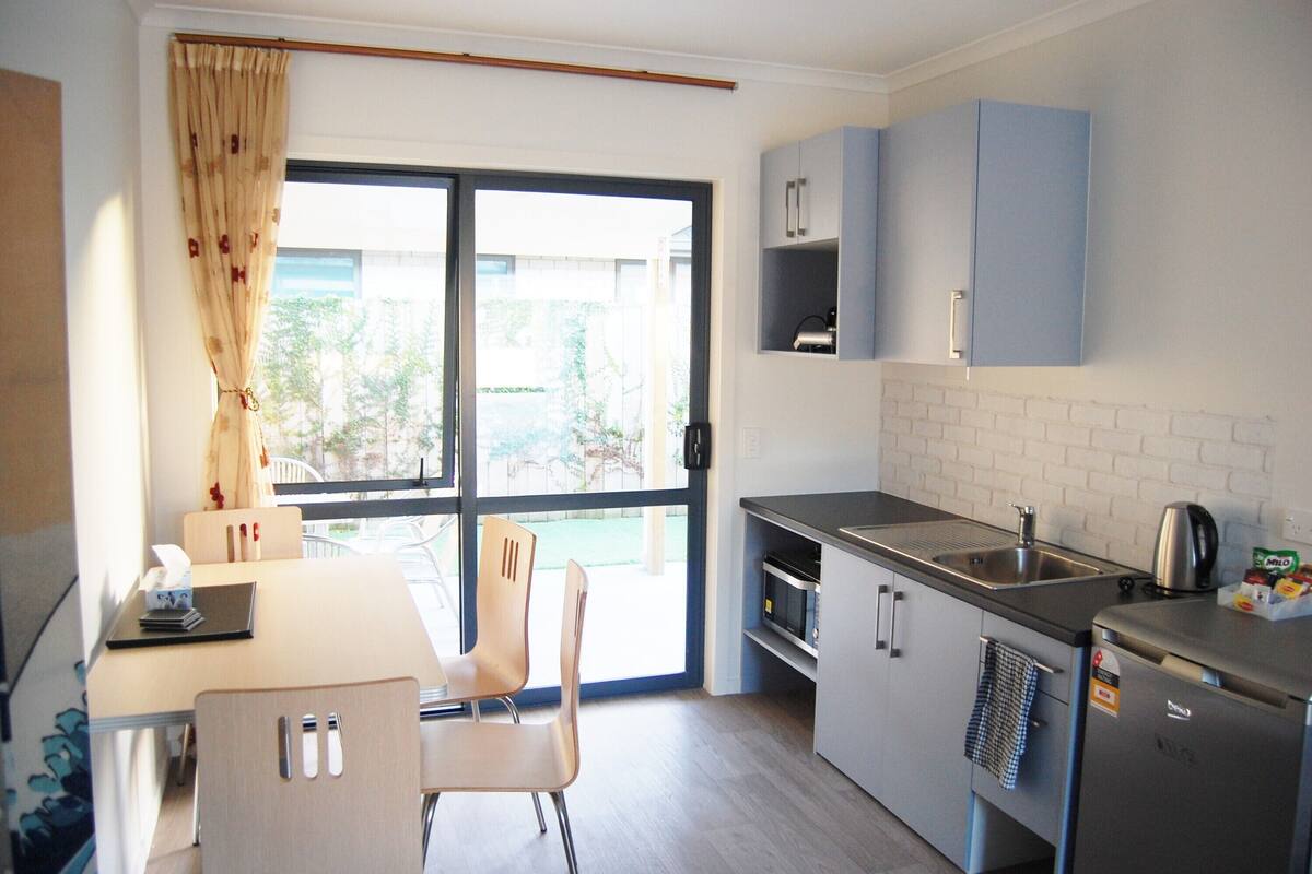 A compact kitchen with a dining area, a sliding glass door leading to a balcony, and a small refrigerator.