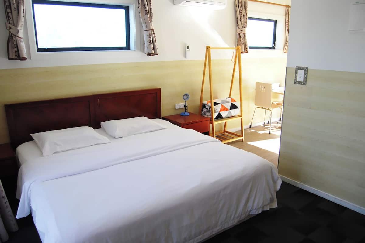 A hotel room with a large bed, a wooden headboard, a bedside table with a lamp, and a window with curtains.
