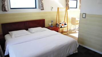 Una habitación de hotel con una cama grande, un cabecero de madera, una mesita de noche con lámpara y una ventana con cortinas.
