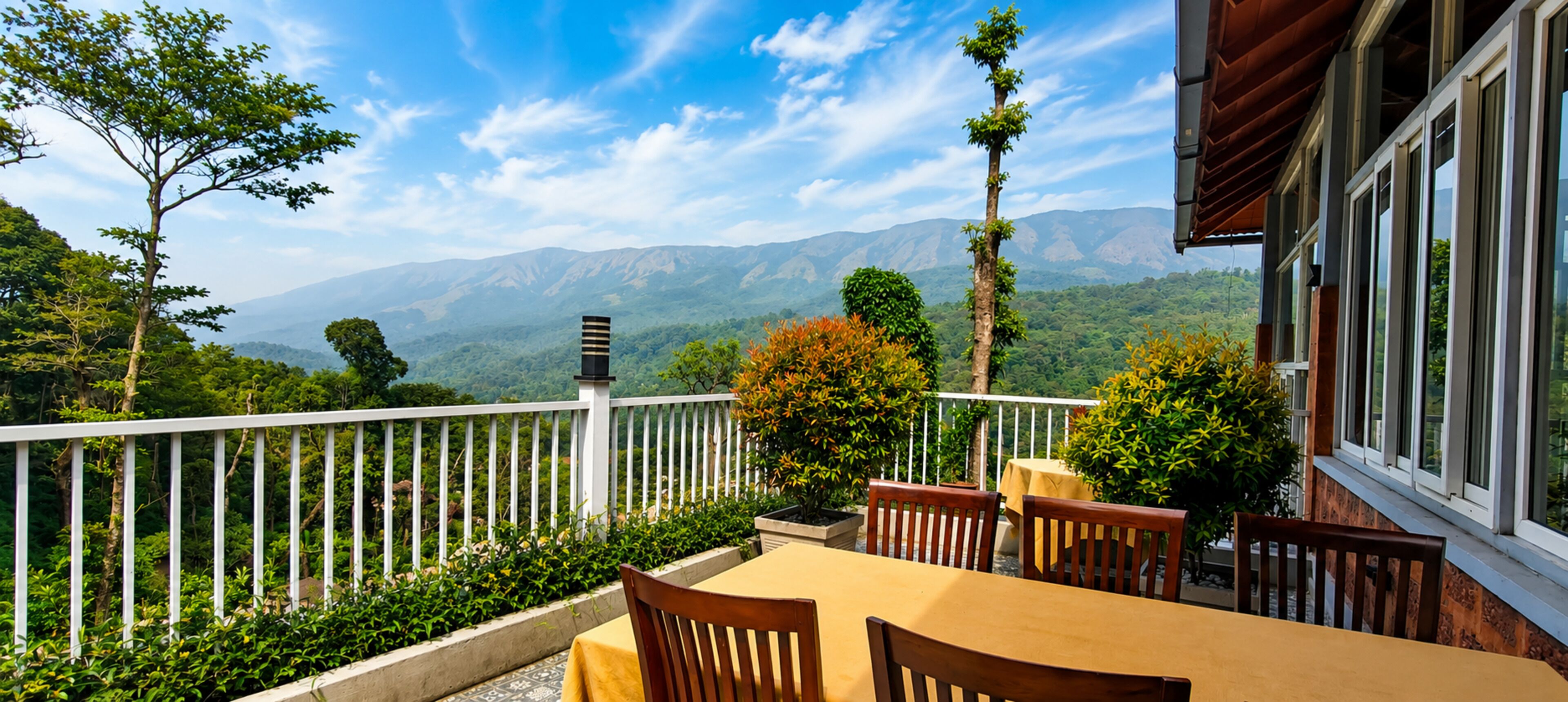Eine Terrasse mit Tisch und Stühlen, einem weißen Geländer und Blick auf Berge.