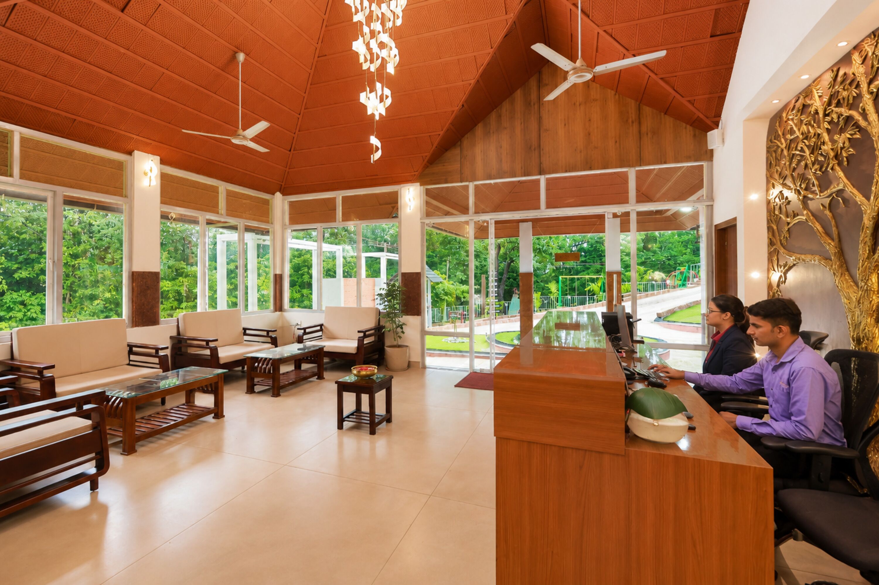 A reception area with a wooden reception desk, seating arrangements, and large windows offering a view of greenery outside.
