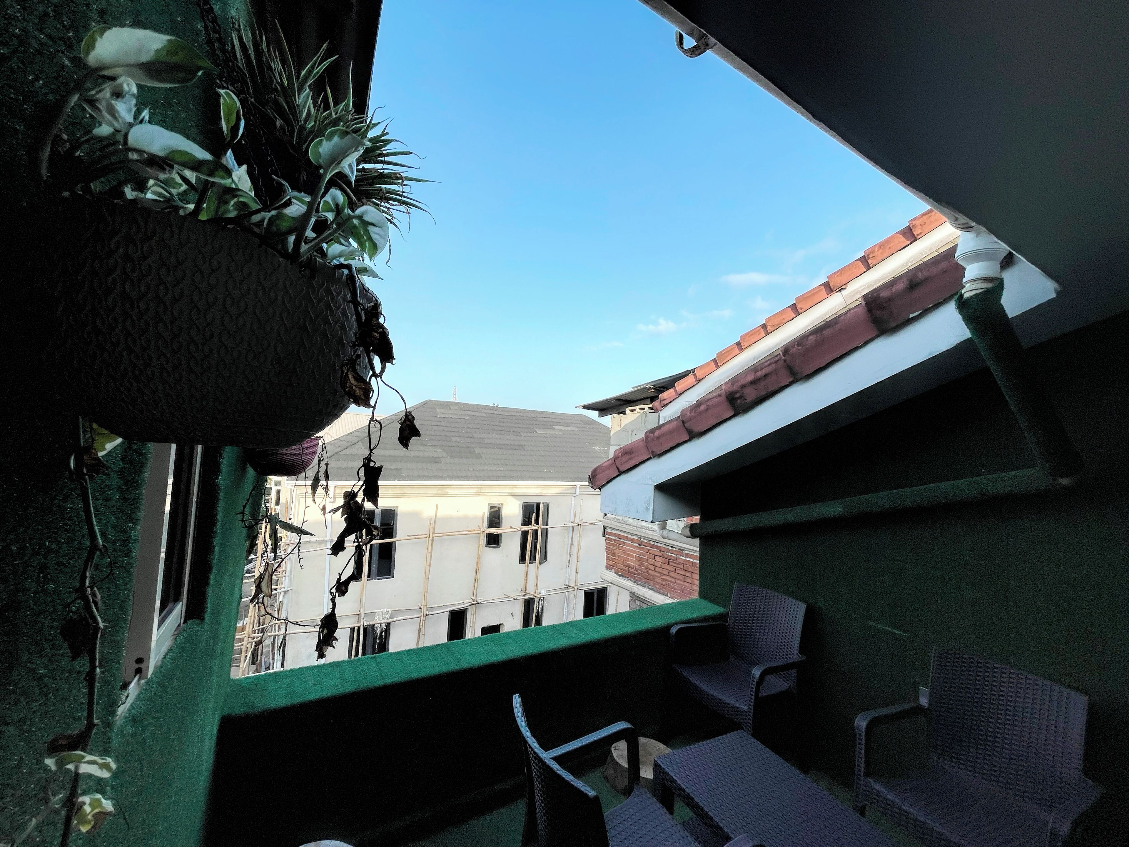 A balcony with a hanging plant, a view of a building with a red roof, and outdoor furniture.