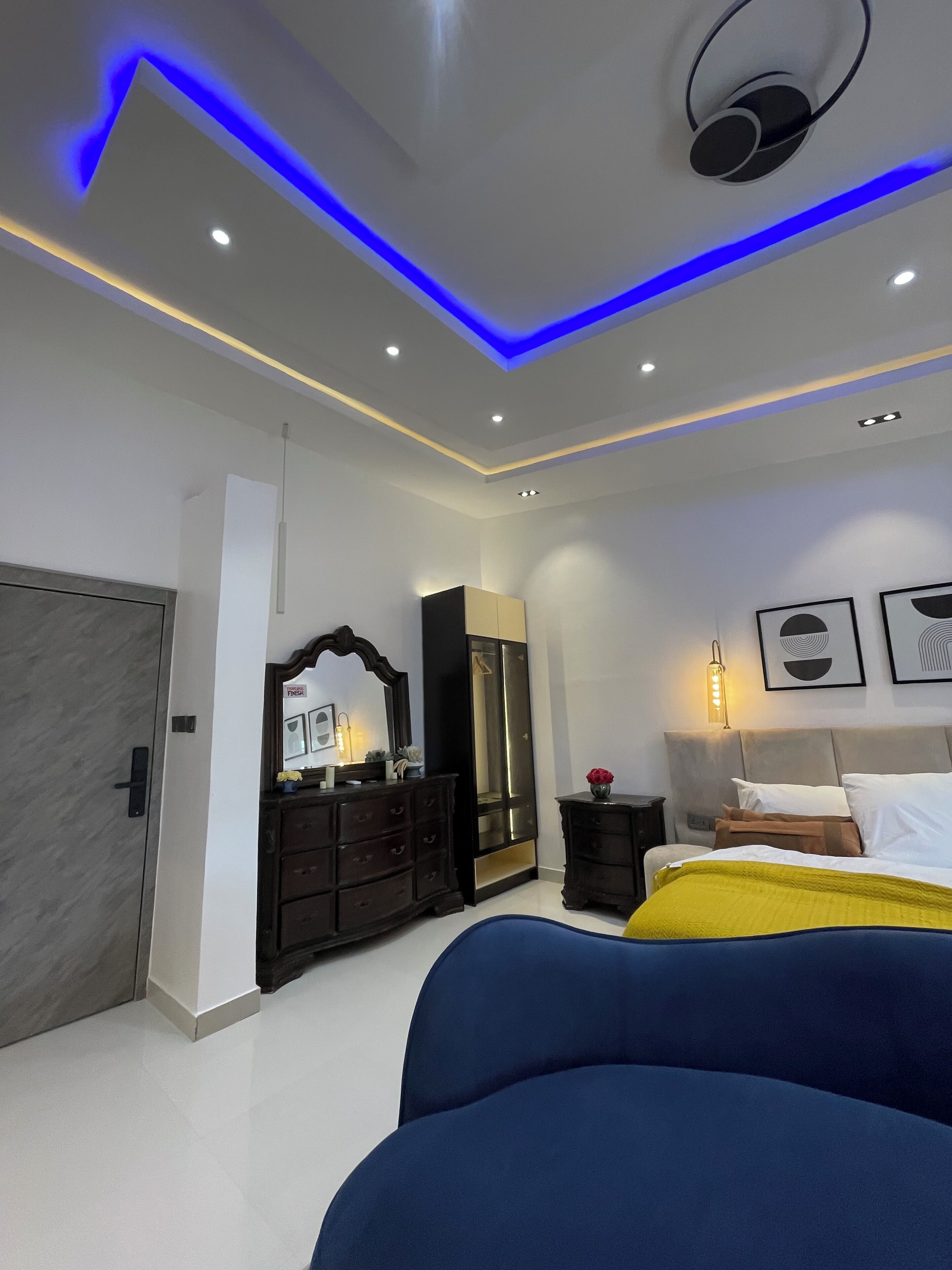 A modern bedroom with a bed, dresser, mirror, and artwork on the walls.