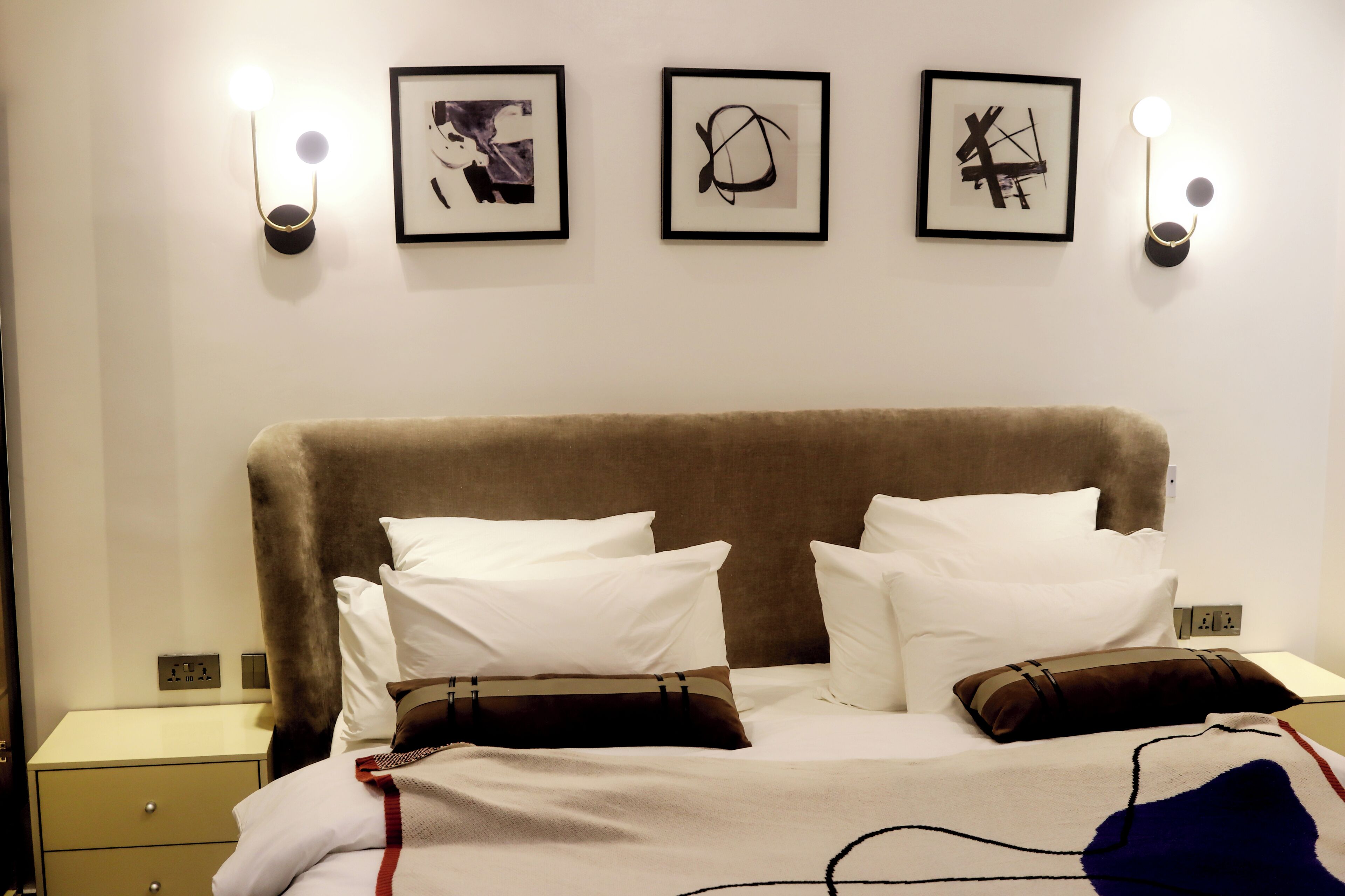 A hotel room with a large bed, two bedside tables, and three framed artworks on the wall.