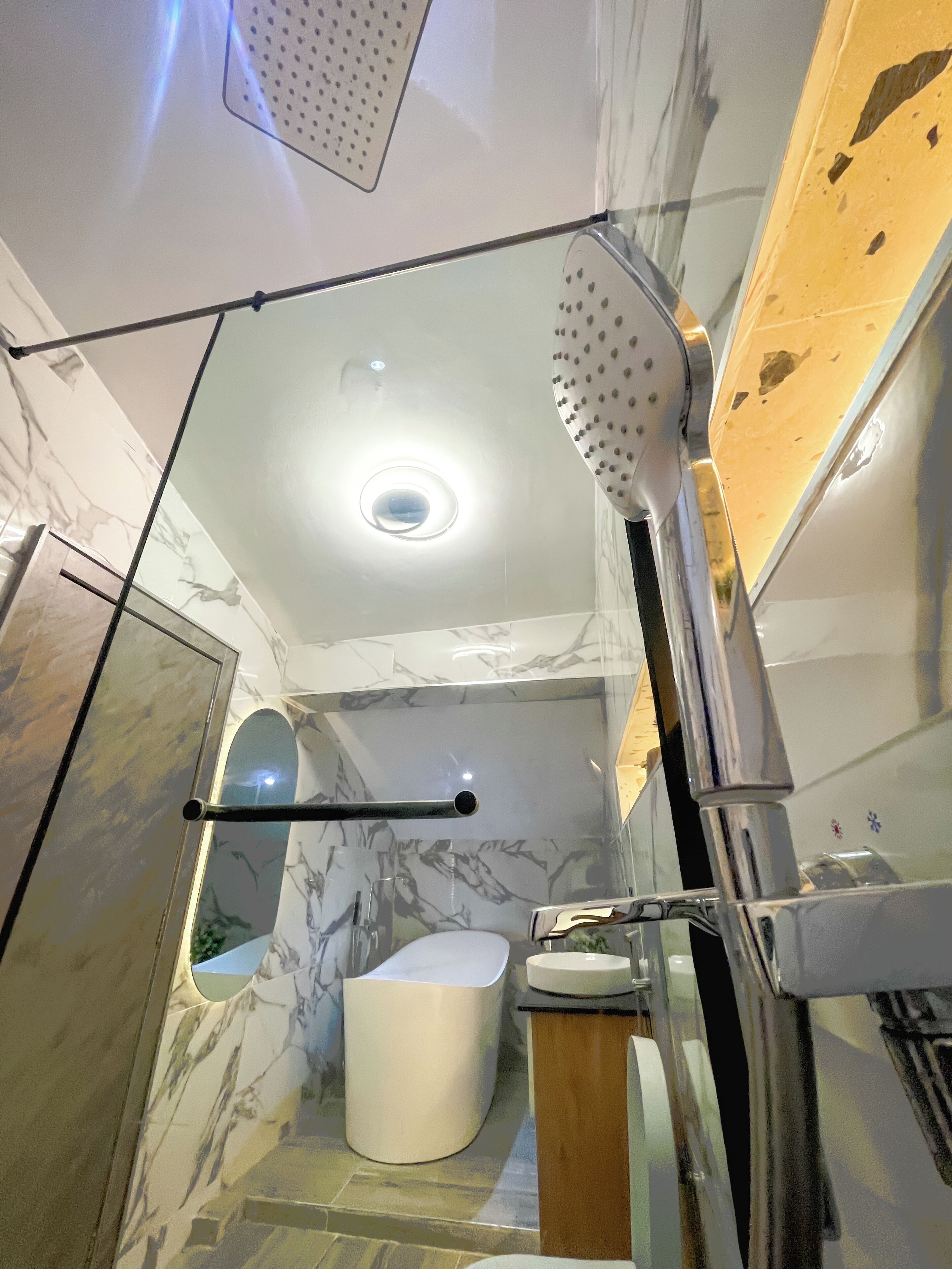 A modern bathroom with a glass shower enclosure, a marble-tiled wall, and a white sink.