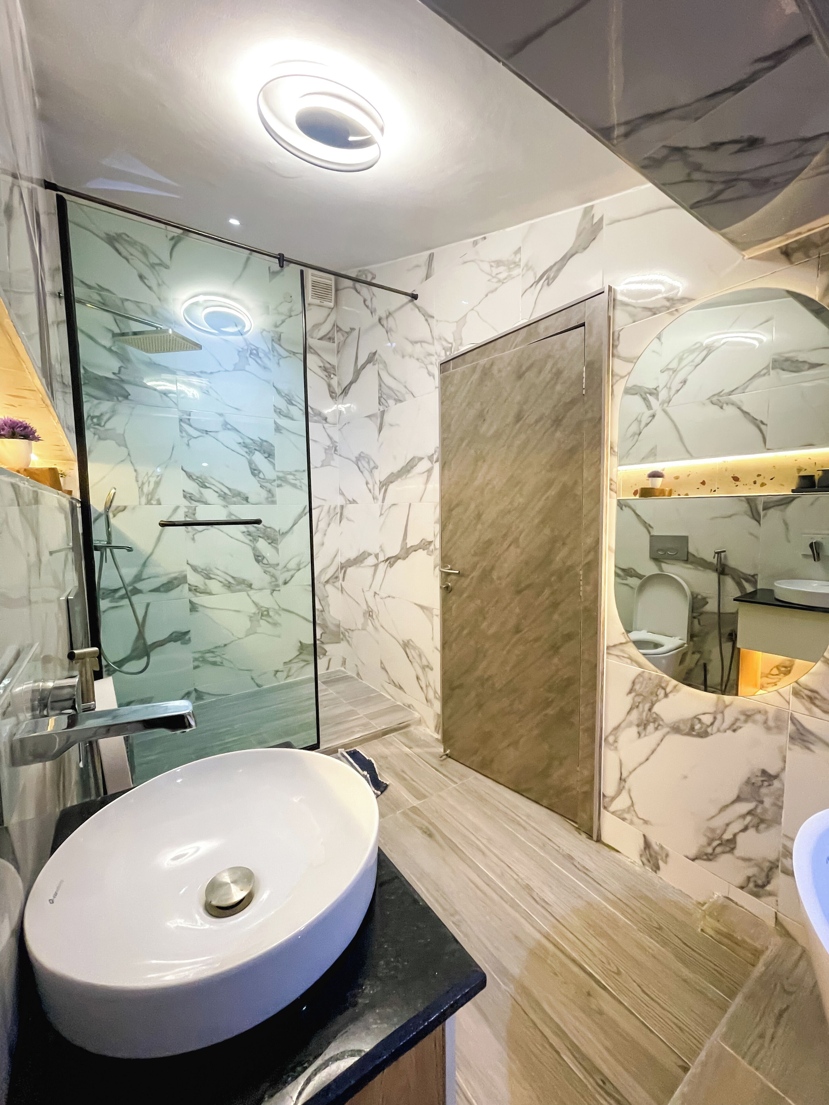 A modern bathroom with a marble vanity, a glass shower enclosure, and a large mirror.