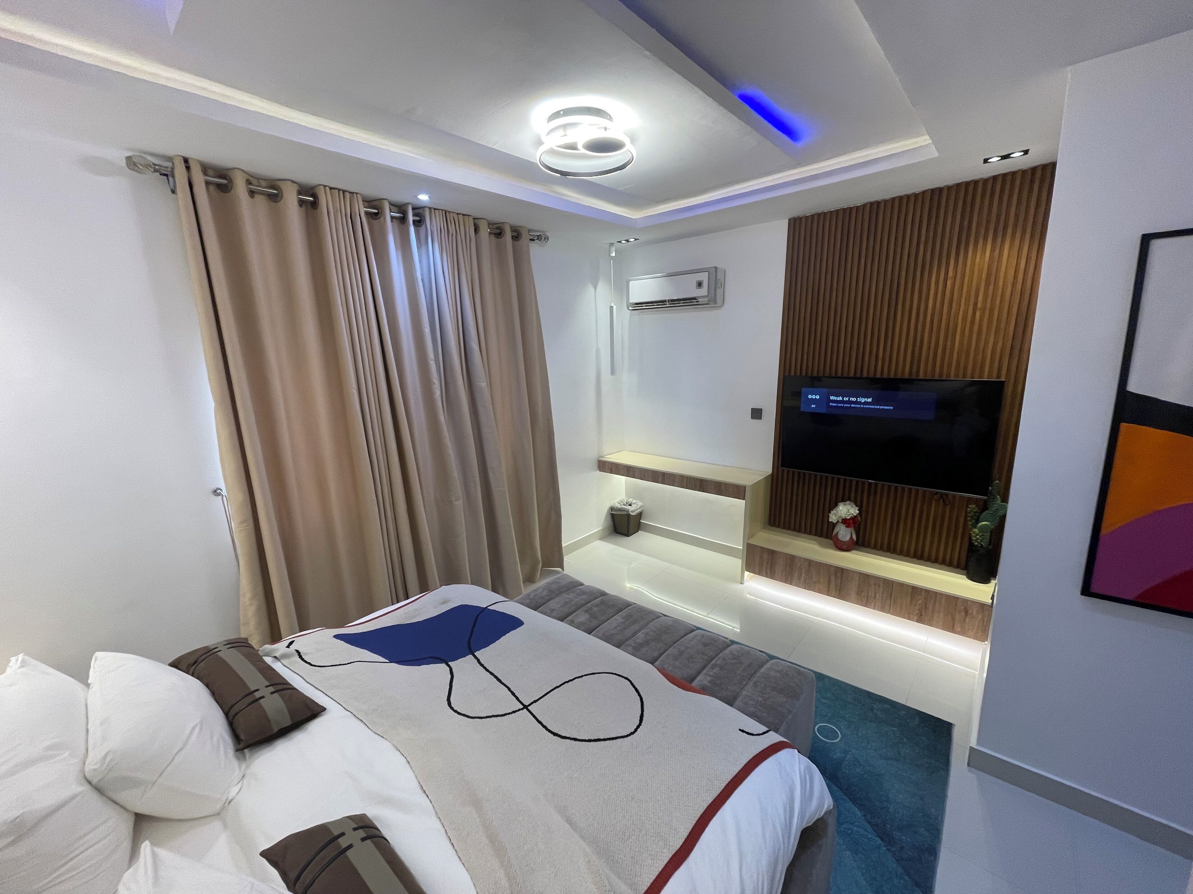 A modern hotel room with a bed, a TV, a bathroom, and a wall-mounted TV.