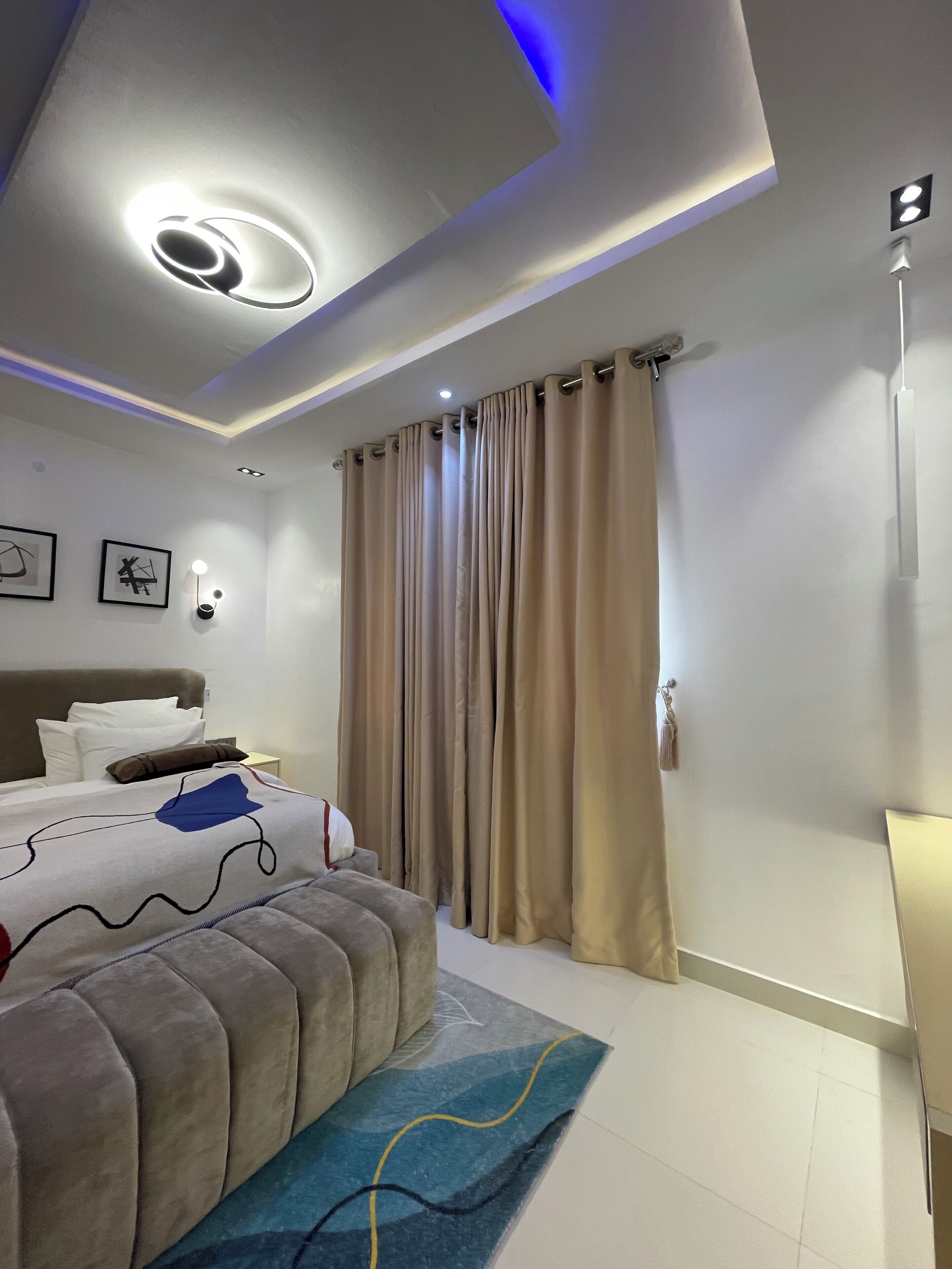 Une chambre moderne avec un lit, des rideaux, une lampe fixée au mur et un luminaire au plafond.