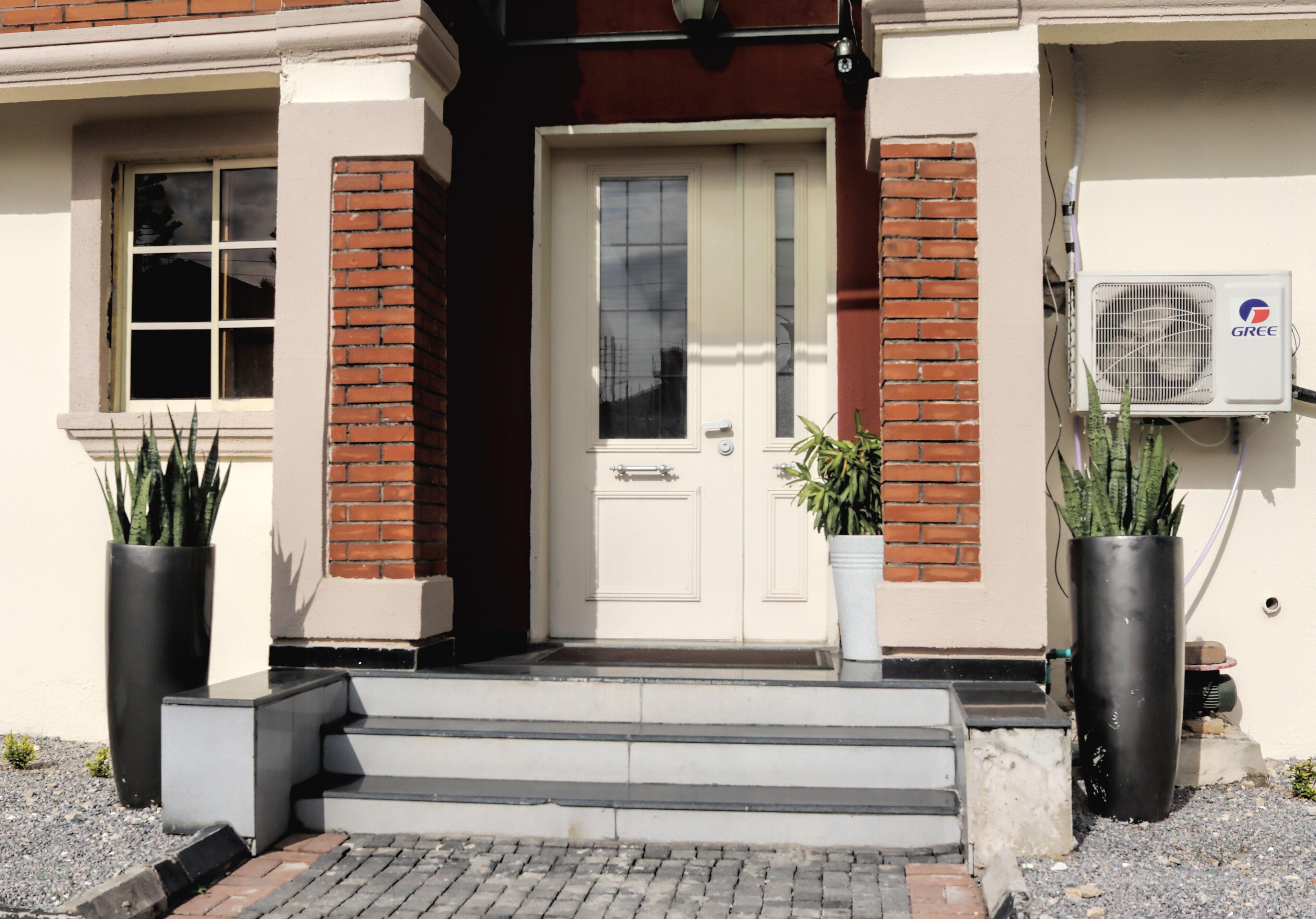 A building entrance with a white door, brick columns, and two potted plants.