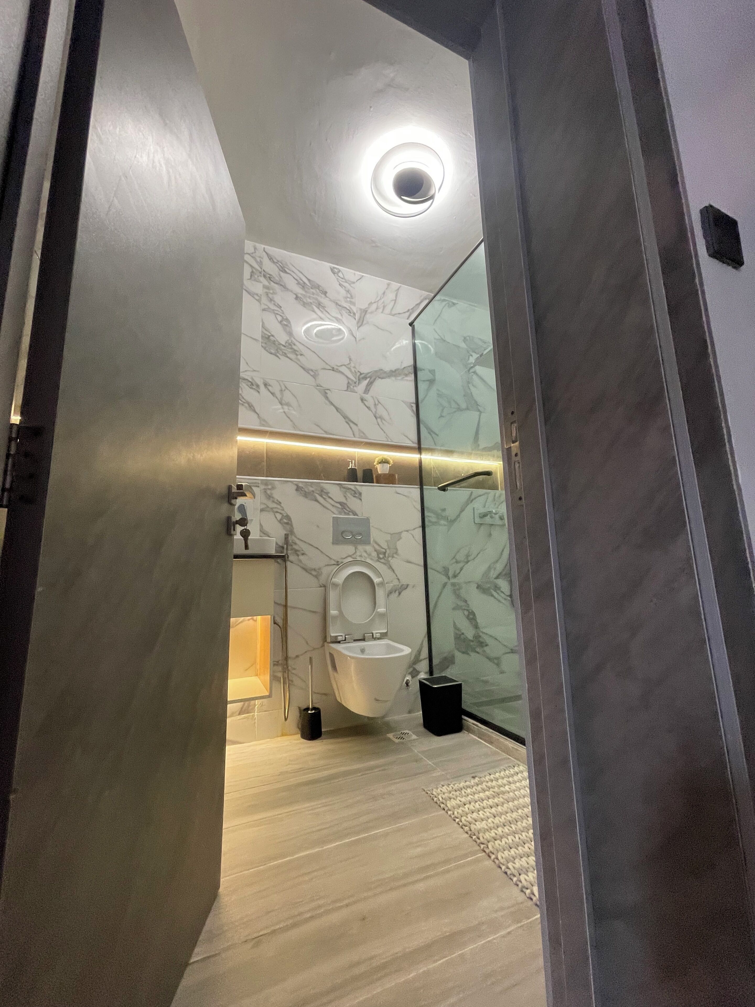 A modern bathroom with a marble wall, a toilet, a bidet, and a glass shower enclosure.