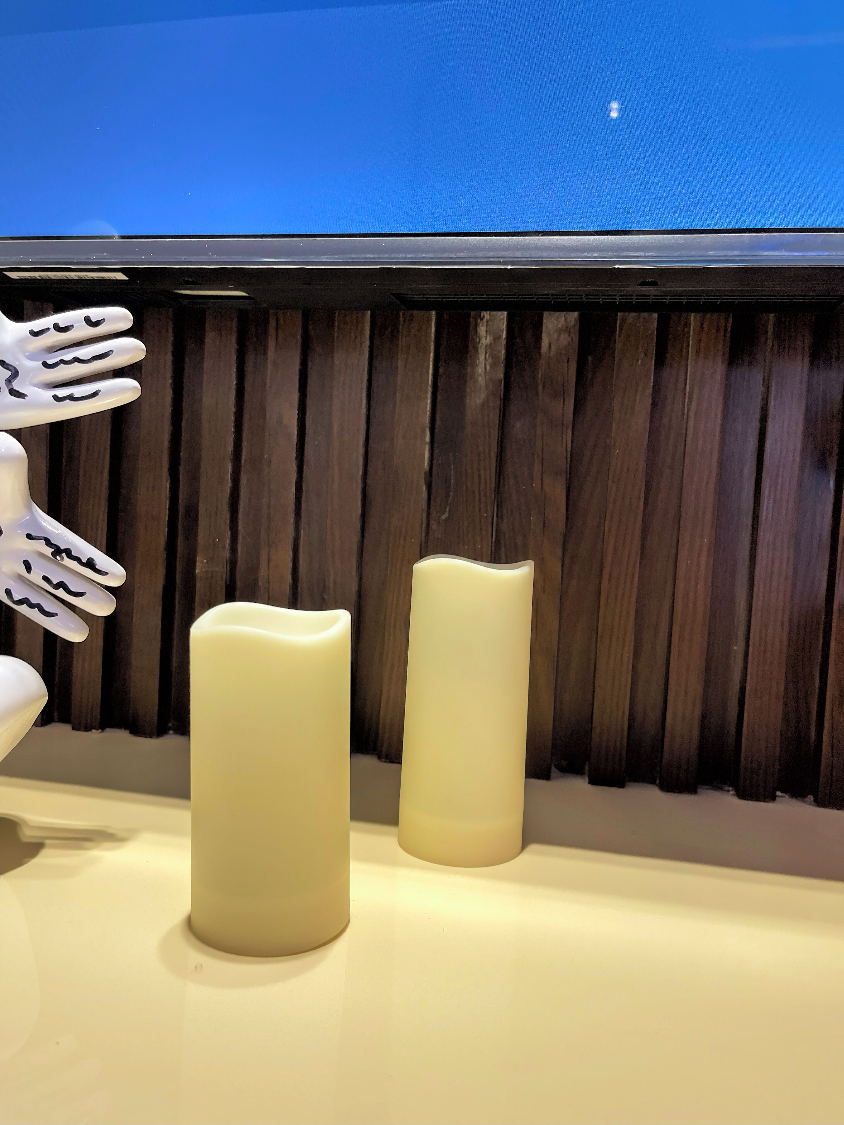 Two white candles on a counter with a wooden panel background.