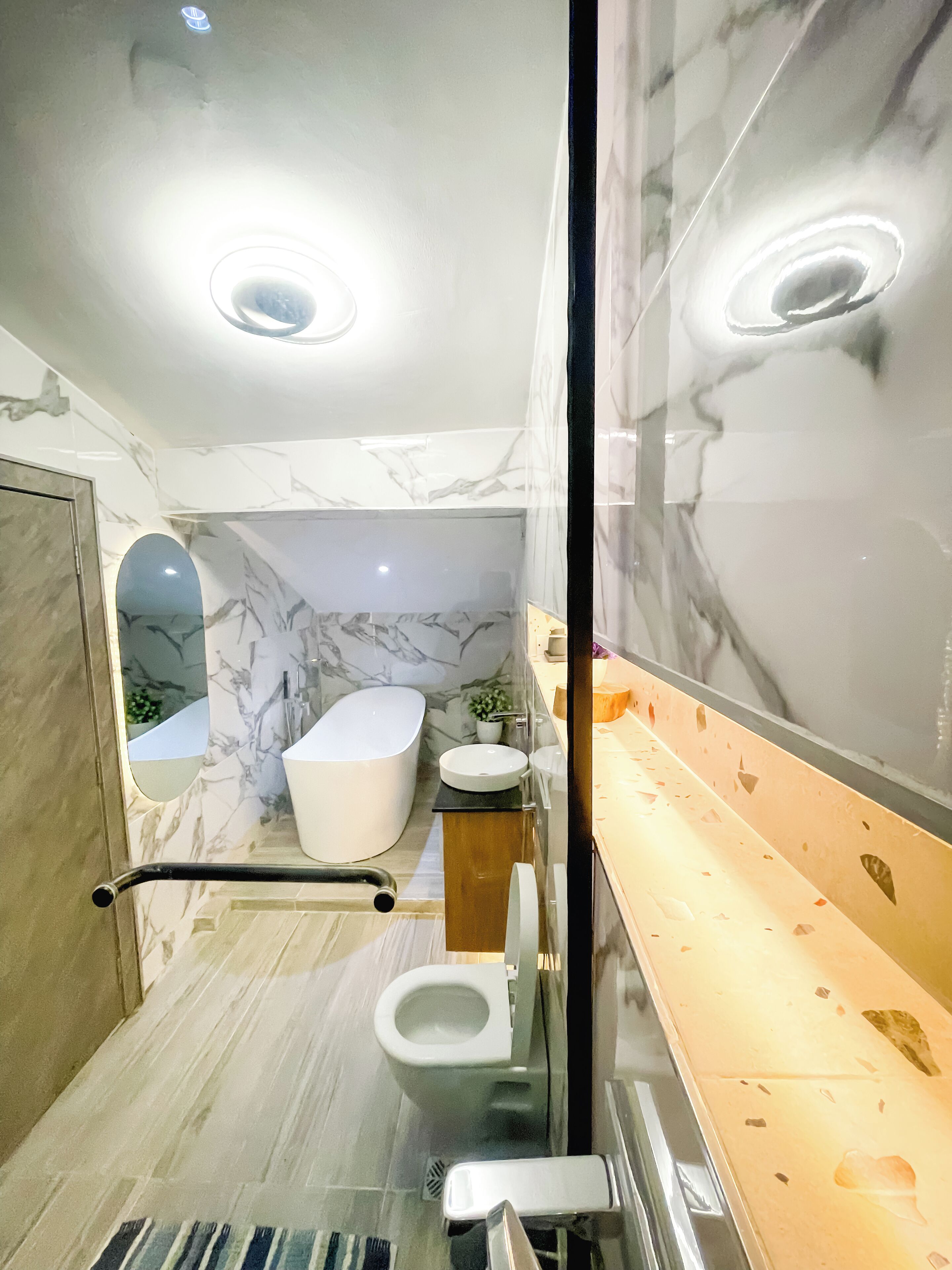 A modern bathroom with a bathtub, toilet, and sink, featuring marble walls and a glass shower enclosure.