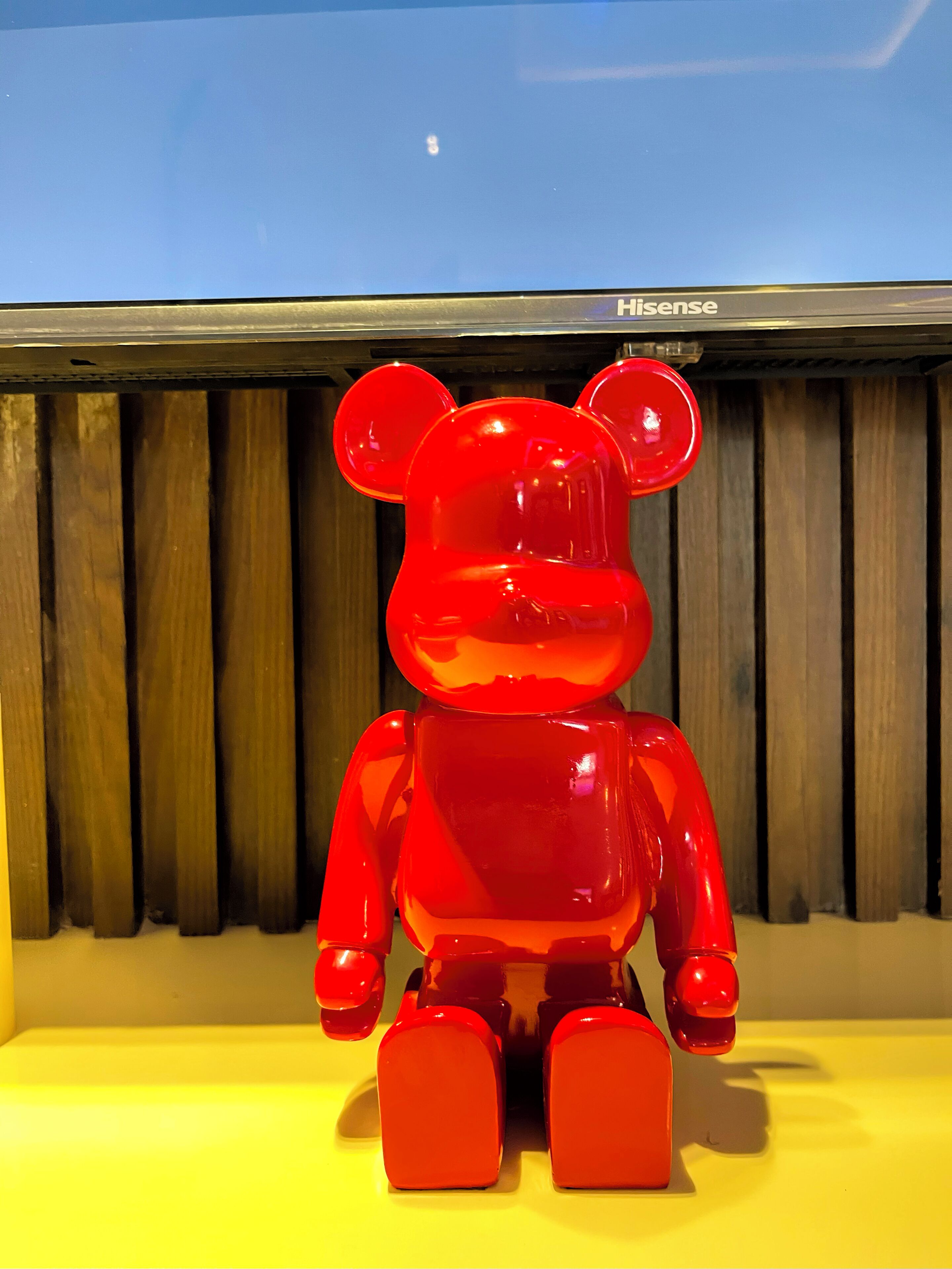 A red bear statue on a yellow surface with a wooden background and a blue sky above.
