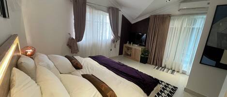 Un dormitorio moderno con una cama grande, un televisor y una pequeña zona de escritorio.