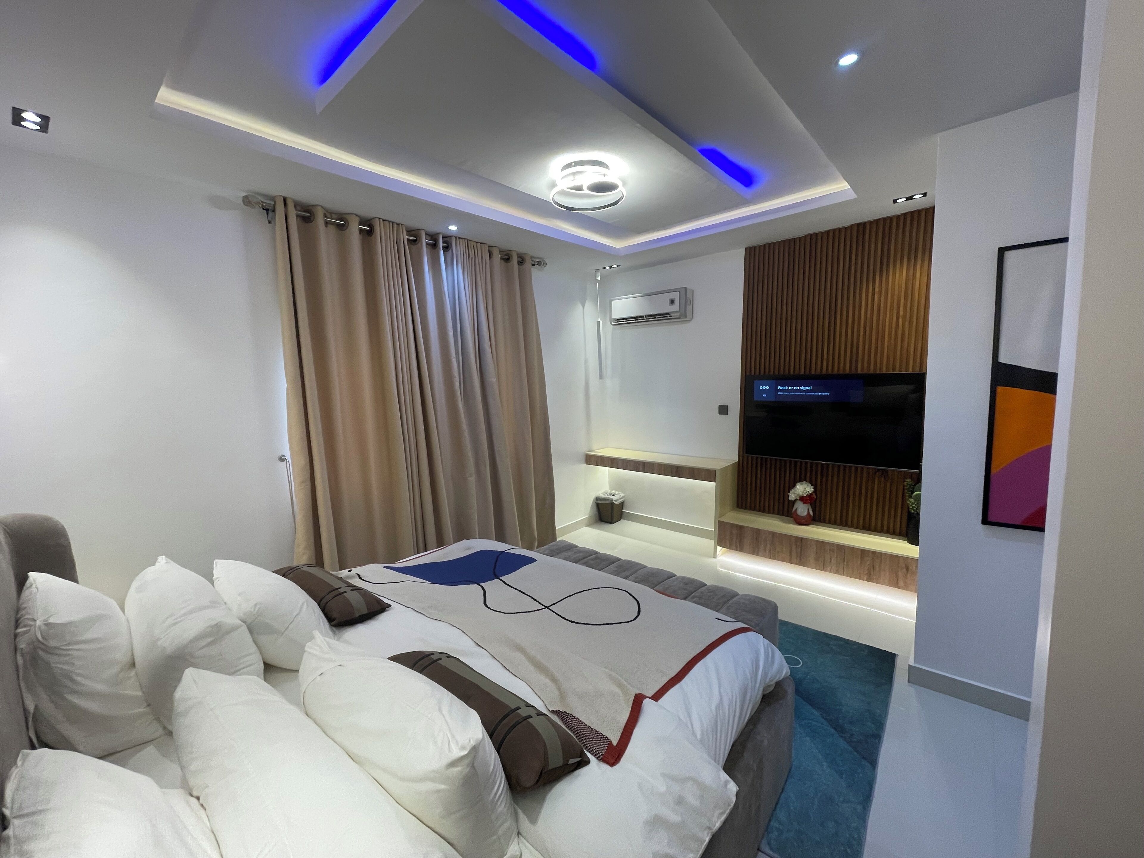 Een moderne hotelkamer met een bed, een flatscreen-tv, een klein nachtkastje en een luchtverkoeler aan de muur.