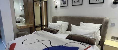 A modern bedroom with a large bed, a wardrobe, a mirror, and wall-mounted lights.