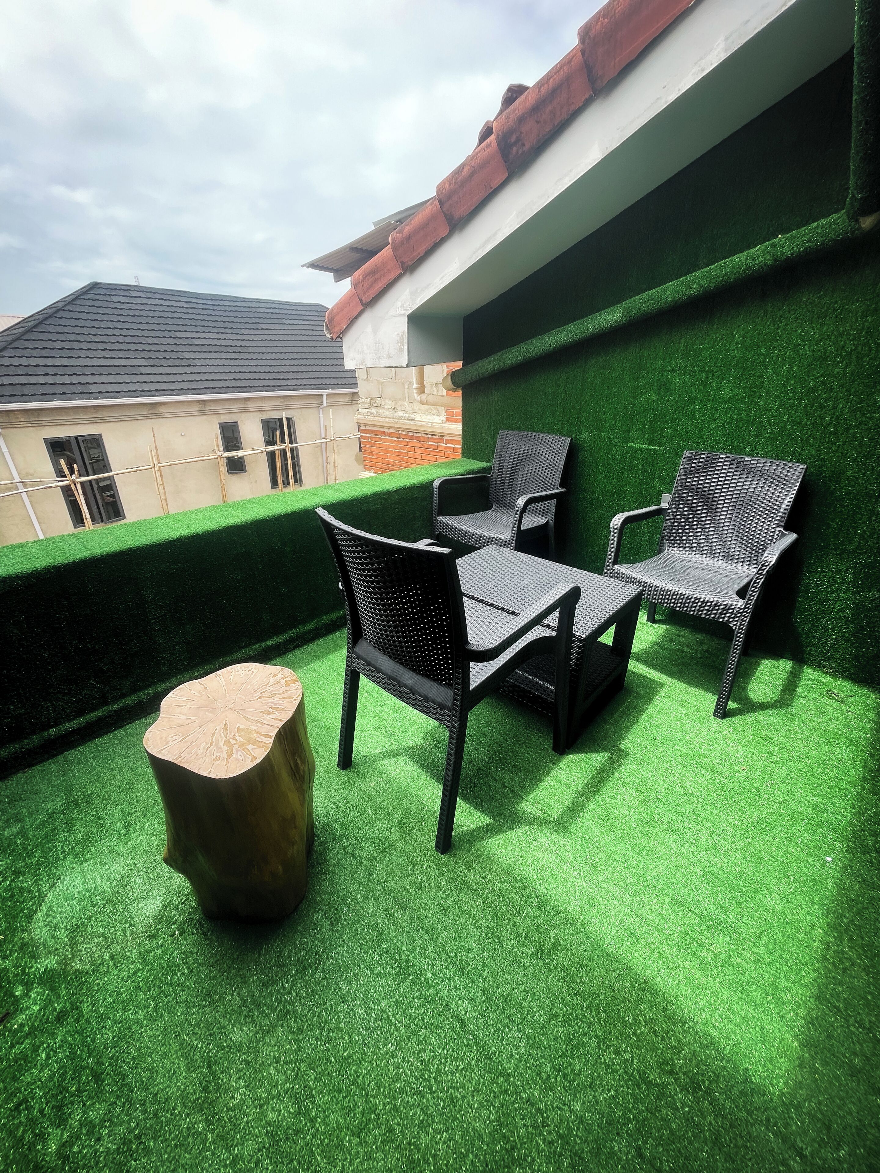 Ein Außenbereich mit Tisch und Stühlen auf Kunstgrifflfläche, ein Holzschemel und eine grüne Wand.