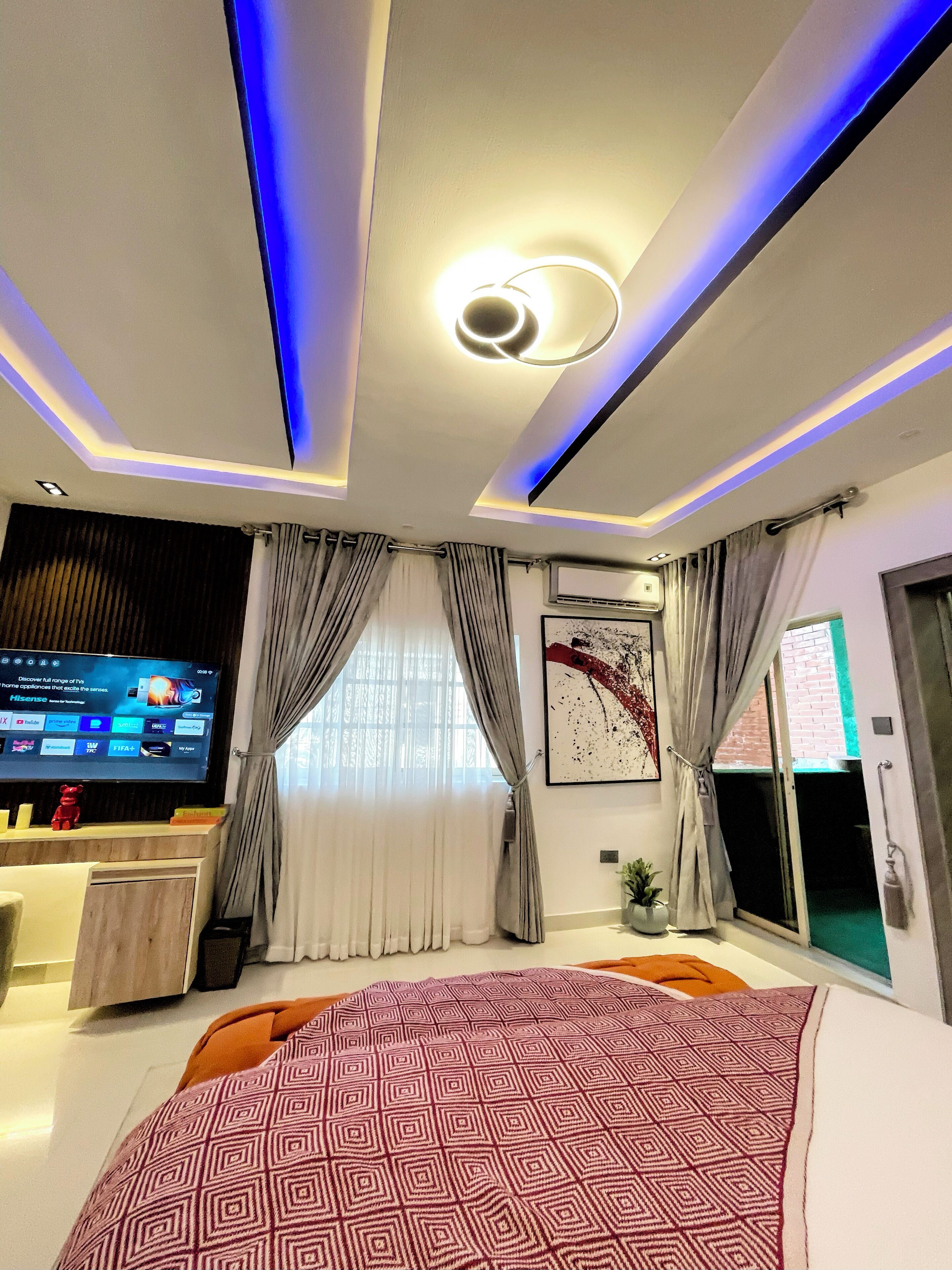 Un dormitorio moderno con una cama grande, un televisor de pantalla plana e iluminación LED azul en el techo.