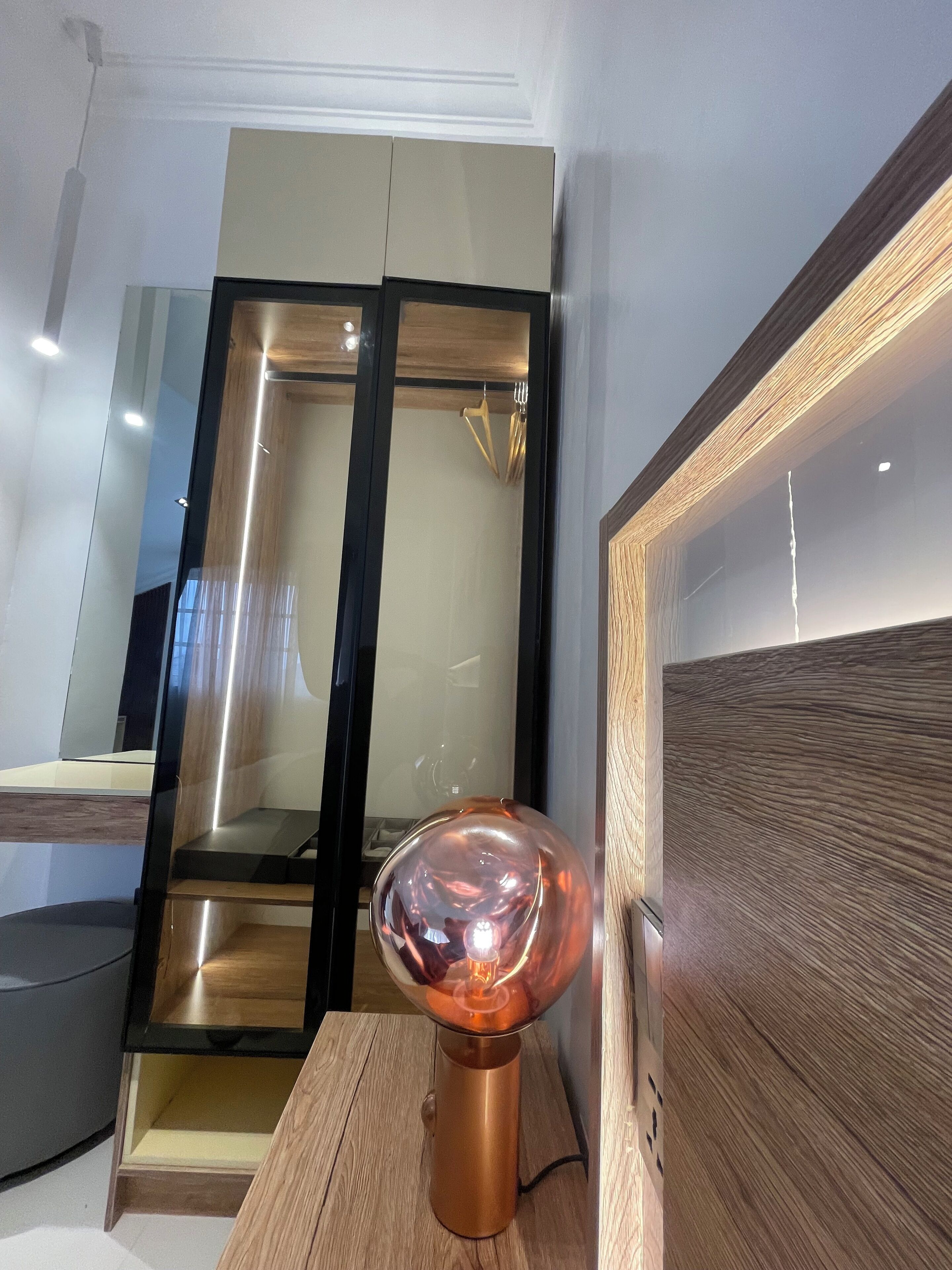 Une pièce moderne avec un plancher en bois, une cloison en verre et une table surmontée d’une lampe de couleur cuivrée.