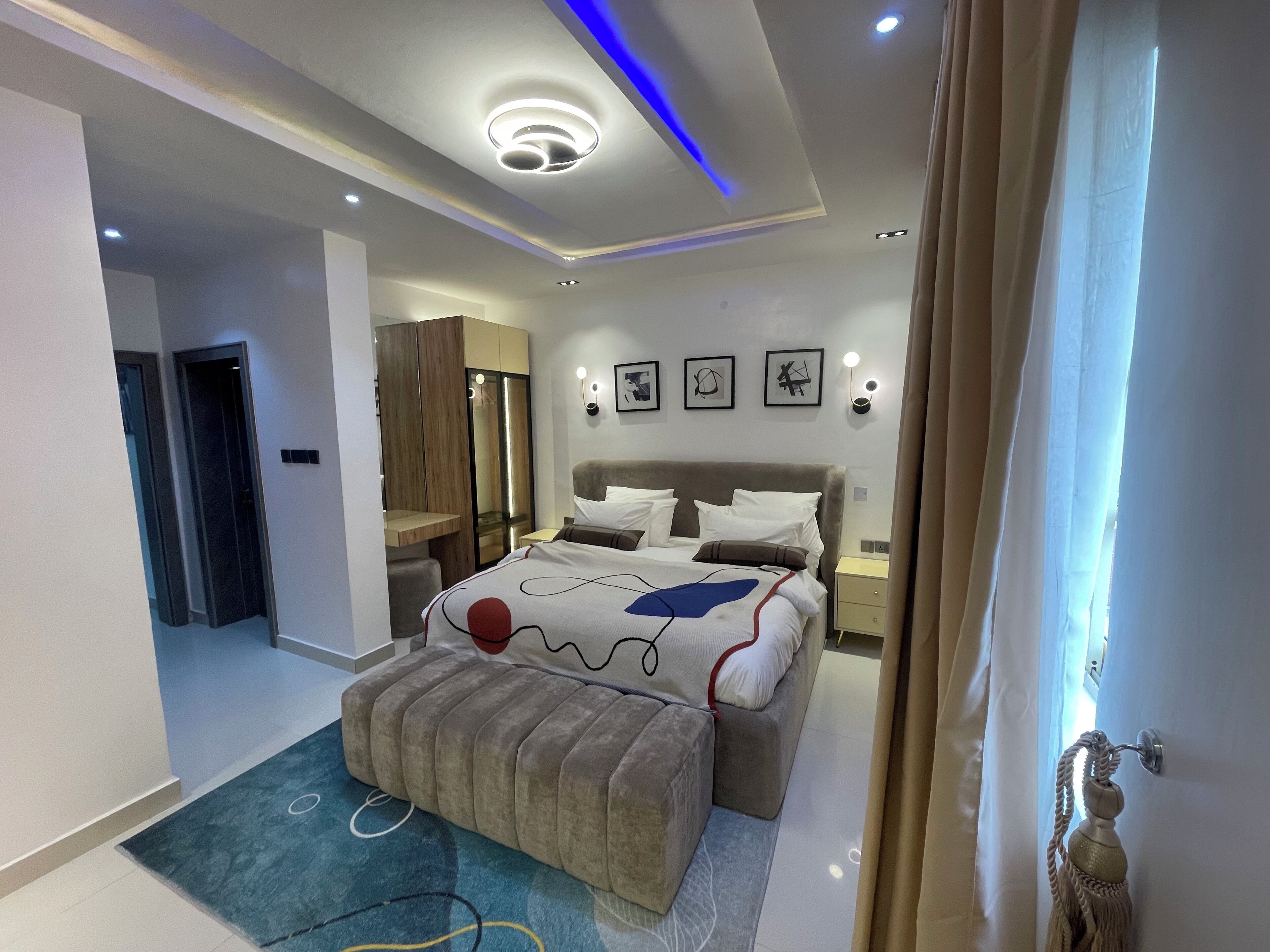 Une chambre d’hôtel moderne, équipée d’un lit, de tables de chevet, d’une armoire et d’une salle de bain visible à travers une porte ouverte.