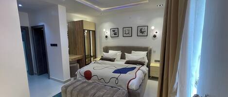 Une chambre d’hôtel moderne, équipée d’un lit, de tables de chevet, d’une armoire et d’une salle de bain visible à travers une porte ouverte.