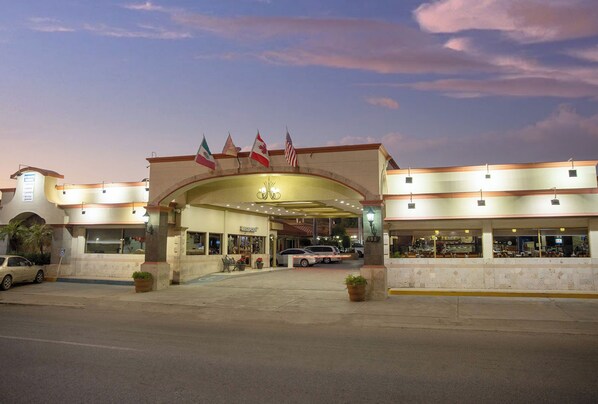A hotel entrance with flags, a covered walkway, and a parking area.