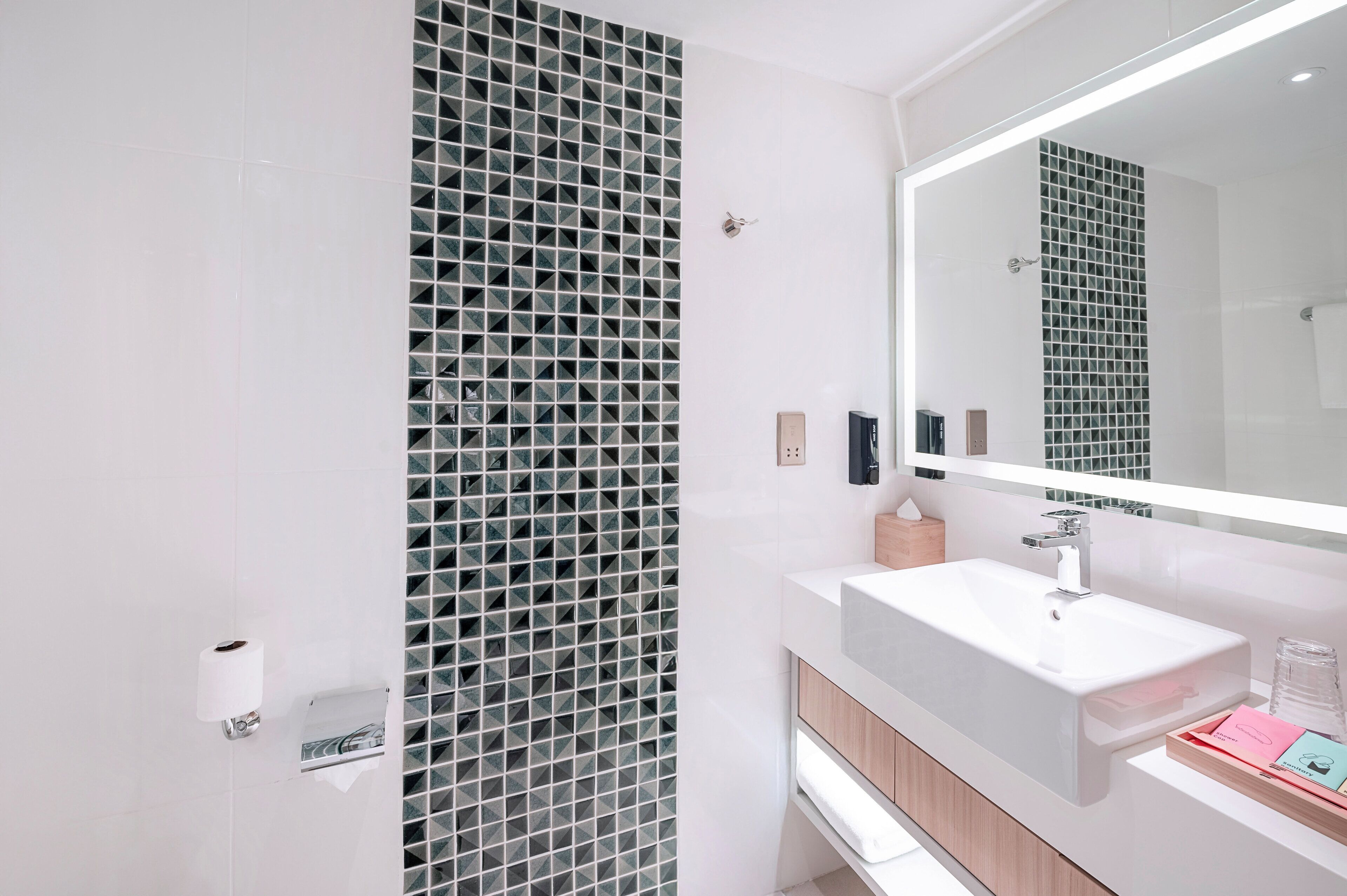 A modern bathroom with a large mirror, a white sink, and a tiled wall.