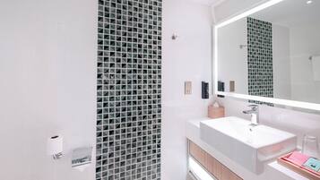 Une salle de bain moderne avec un grand miroir, un lavabo blanc et un mur recouvert de carreaux.