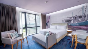 Hotelkamer met een bed, een bank, een tafeltje en een stoel. Er is een groot raam met gordijnen en een schilderij aan de muur.