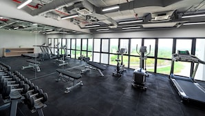 Een sportschool met trainingsapparatuur, grote ramen en uitzicht op de omgeving.