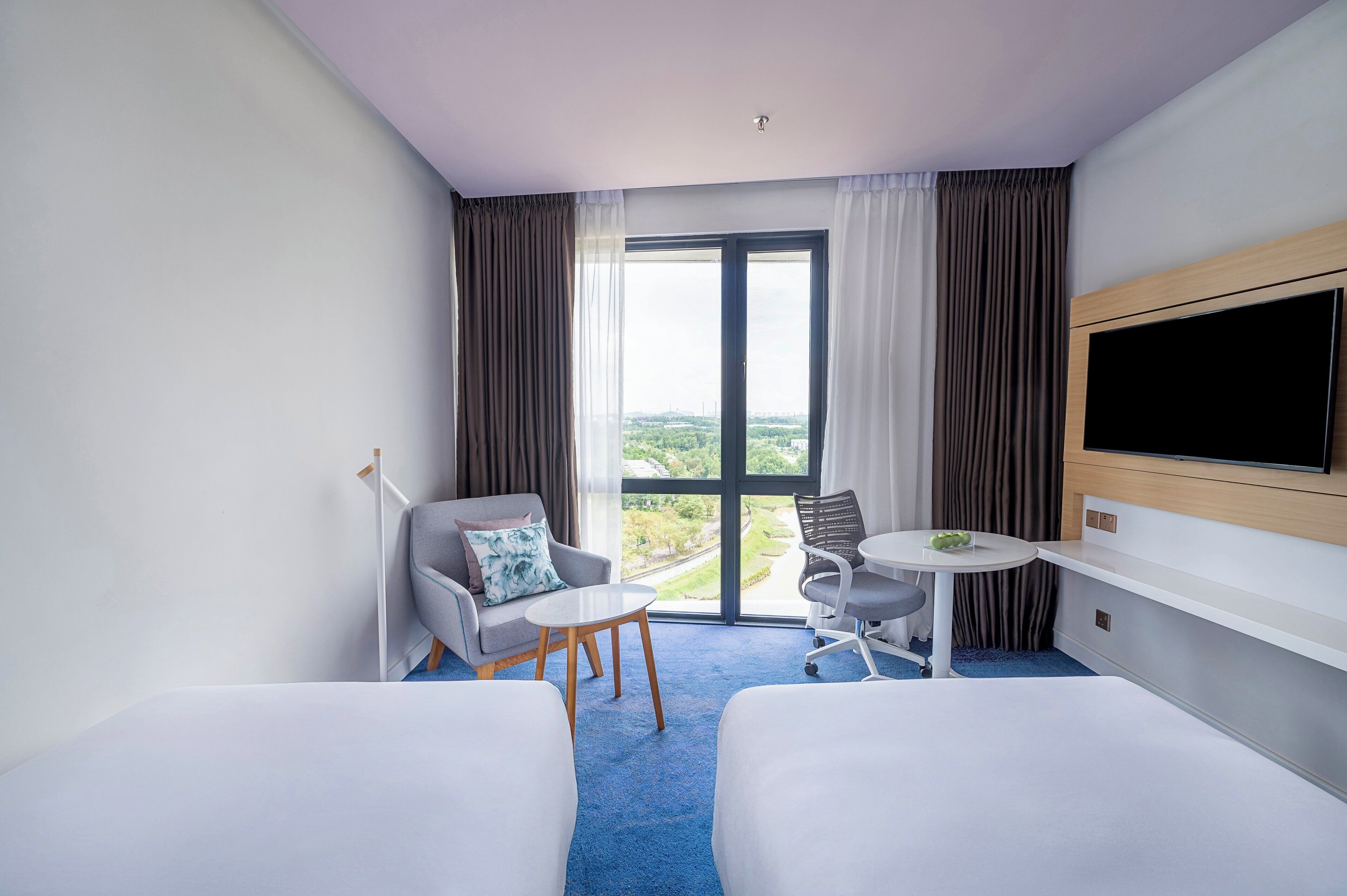 Habitación de hotel con dos camas, un televisor, una mesita y vistas a la ciudad.