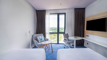 Habitación de hotel con dos camas, un televisor, una mesita y vistas a la ciudad.