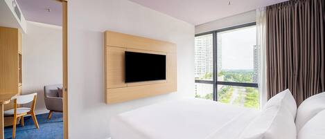 Une chambre d’hôtel avec un grand lit, un téléviseur fixé au mur, un bureau avec une chaise et une vue sur le paysage urbain par la fenêtre.