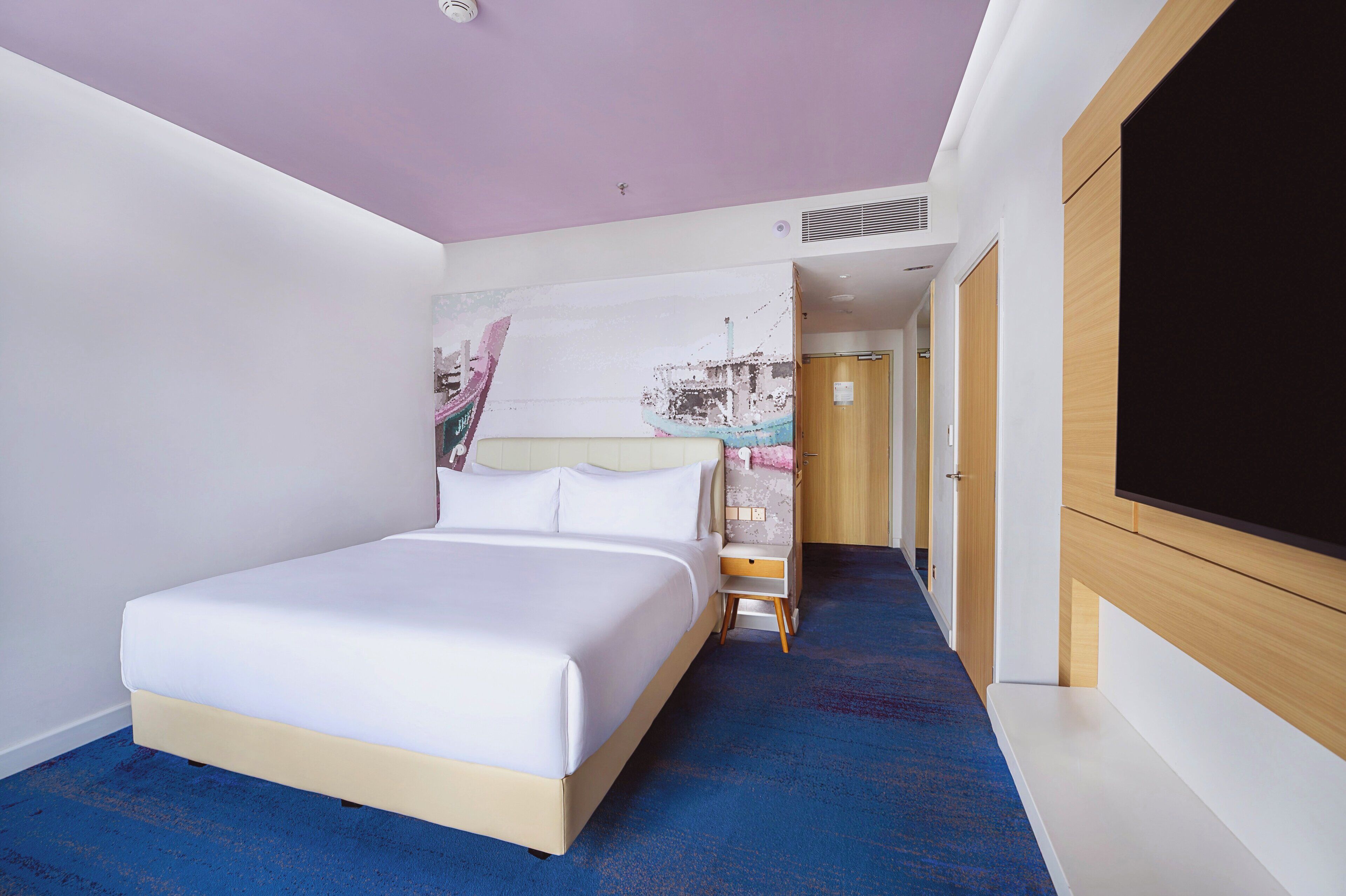 Una habitación de hotel con cama, un escritorio pequeño, televisión y un pasillo que lleva a otra habitación.