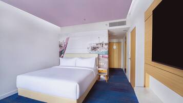 Una habitación de hotel con cama, un escritorio pequeño, televisión y un pasillo que lleva a otra habitación.