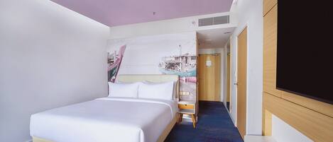 Una habitación de hotel con cama, un escritorio pequeño, televisión y un pasillo que lleva a otra habitación.