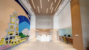 Een ruime lobby met een modern receptiebalie, een muurschildering van een klokkentoren en een hoog plafond met lineaire verlichting.