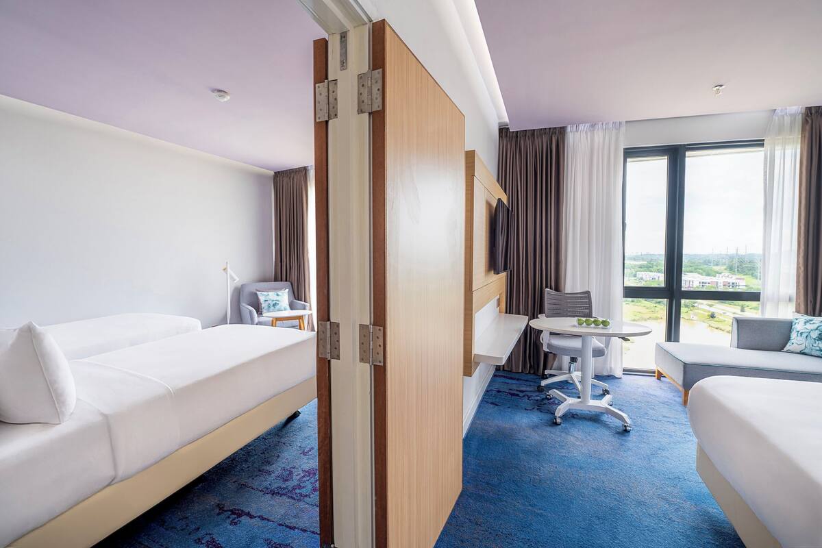 Une chambre d’hôtel avec deux lits, un bureau, une chaise et une vue sur l’extérieur.