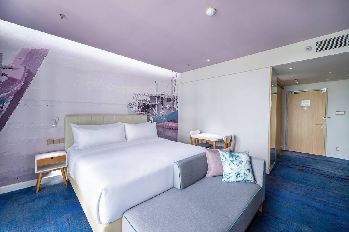 Ein modernes Hotelzimmer mit einem großen Bett, einer kleinen Sitzecke, einem Schreibtisch und einer Badezimmertür.