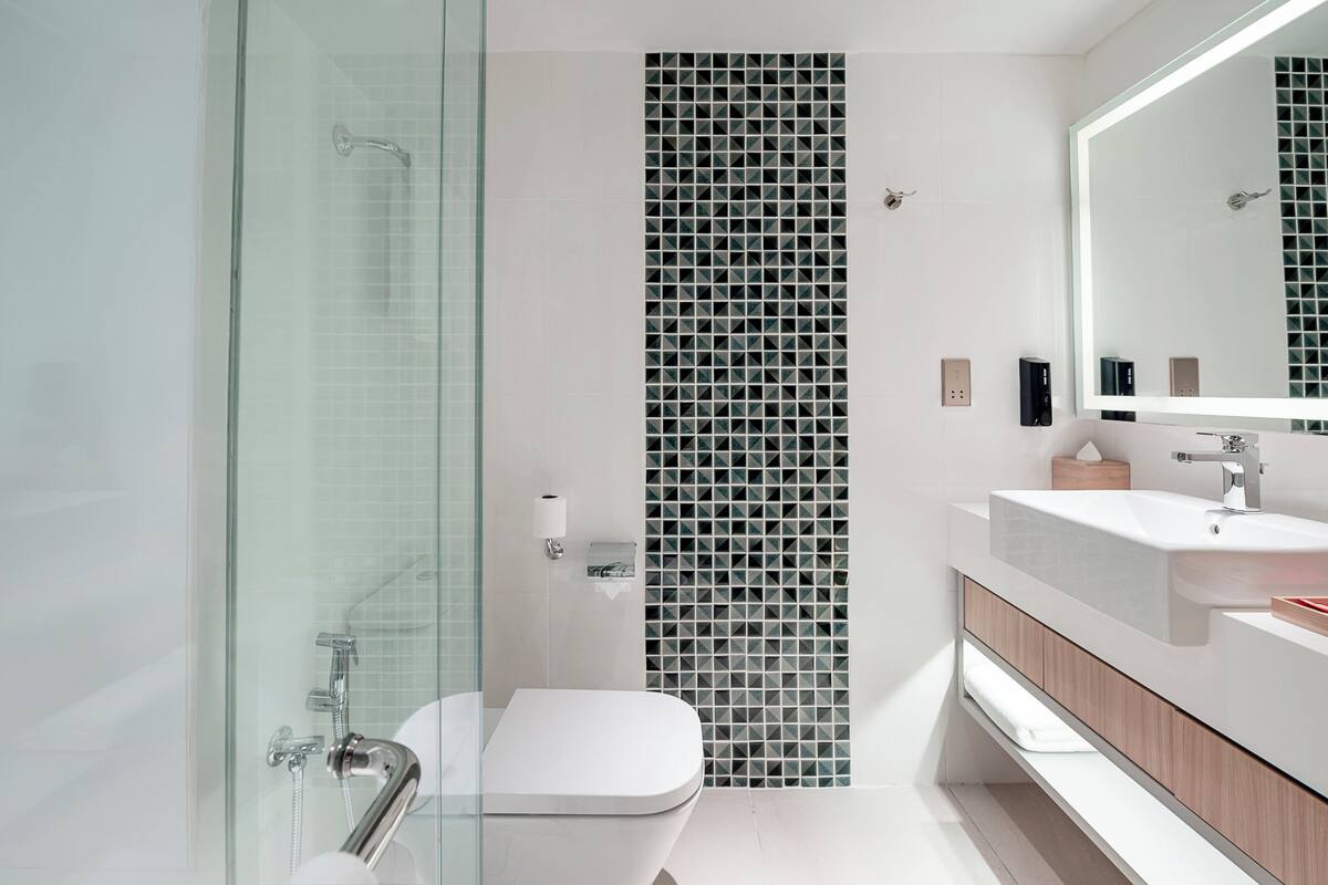 Ein modernes Badezimmer mit Duschkabine aus Glas, weißer Toilette, Waschbecken mit Spiegel und gefliesten Wänden.