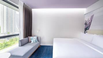 A modern hotel room with a large bed, a sofa with a view, and a painting on the wall.