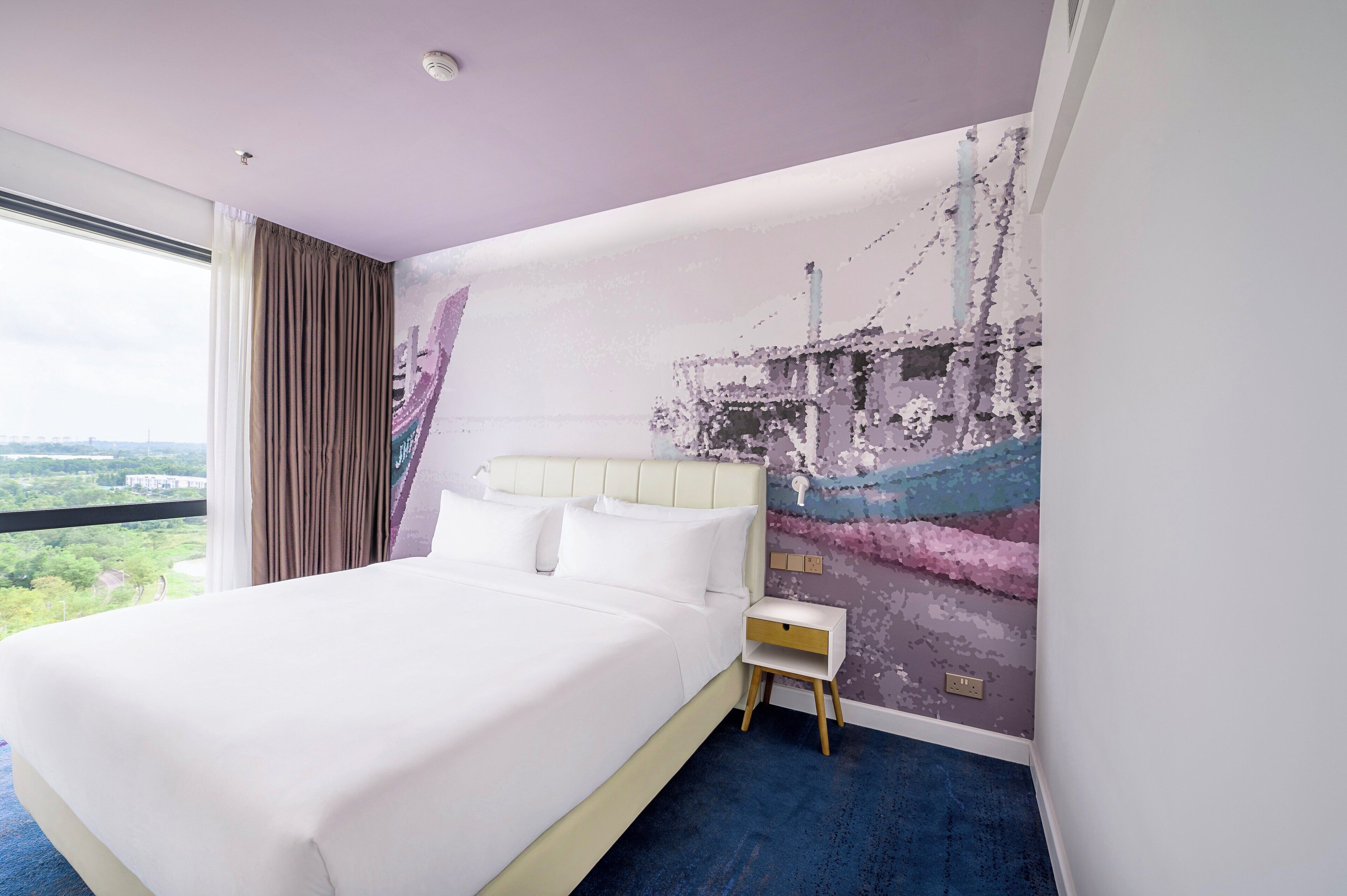 Una habitación de hotel con una cama grande, una mesita de noche, un mural en la pared y vistas de la ciudad.