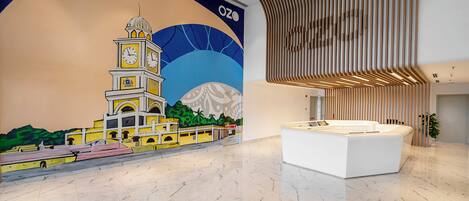 A modern lobby with a mural of a clock tower, a reception desk, and a wooden slatted ceiling.
