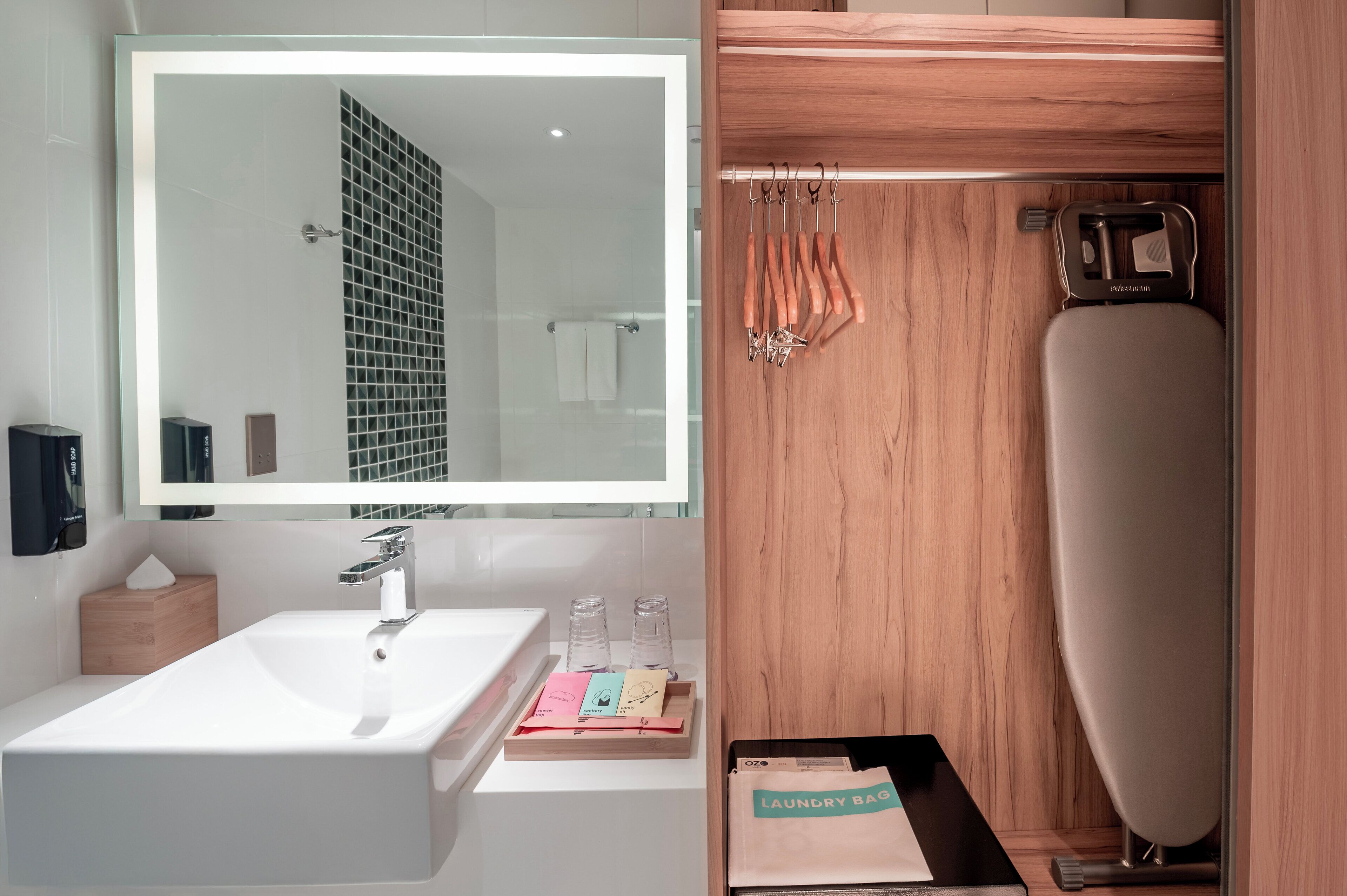 A modern bathroom with a large mirror, a white sink, and a wooden vanity.