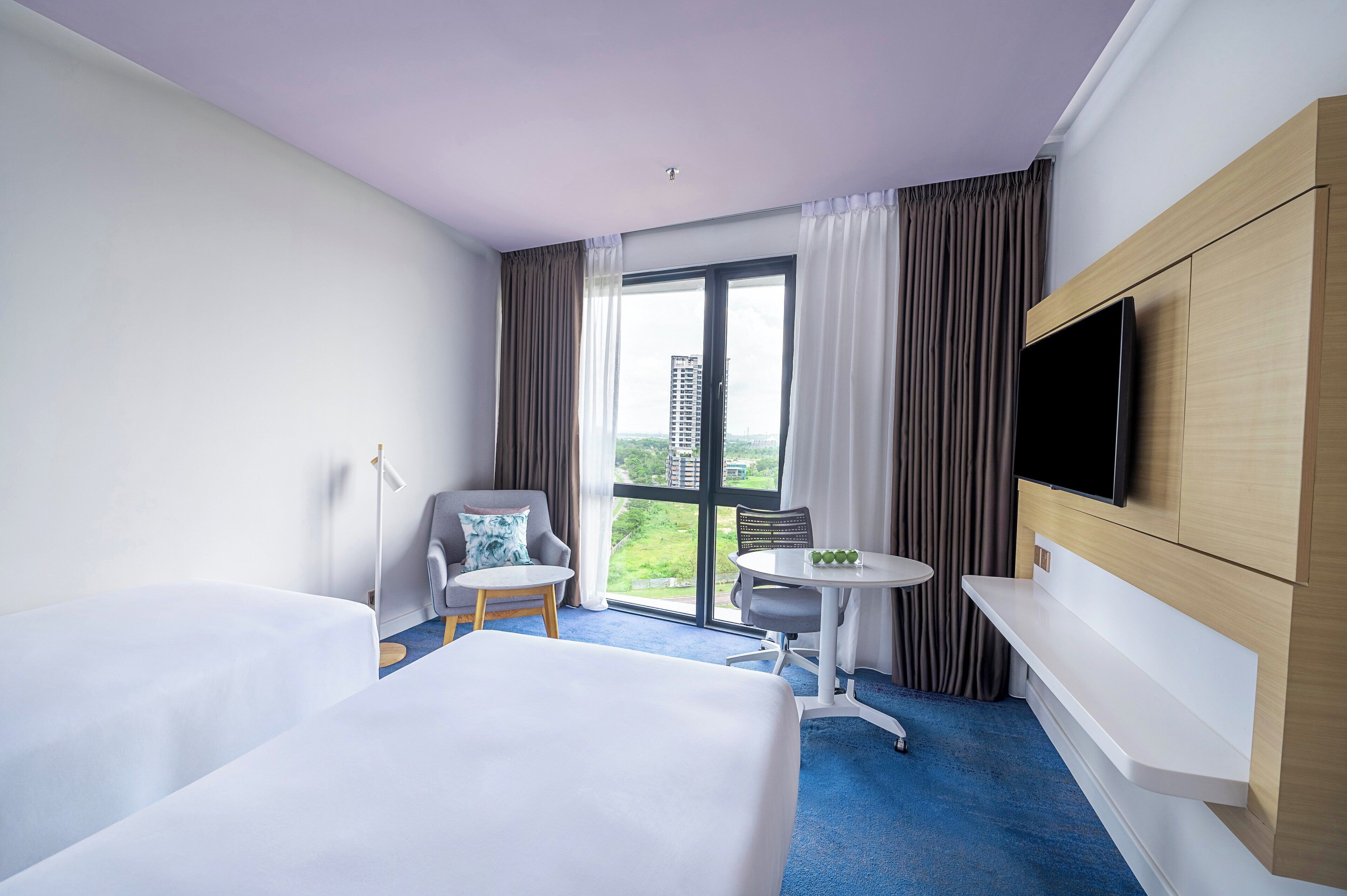A hotel room with two beds, a TV mounted on the wall, a small table, and a chair.